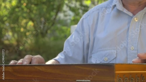 Old gray-haired man opens the chess game outside in the garden at the table and puts the black figures side by side.