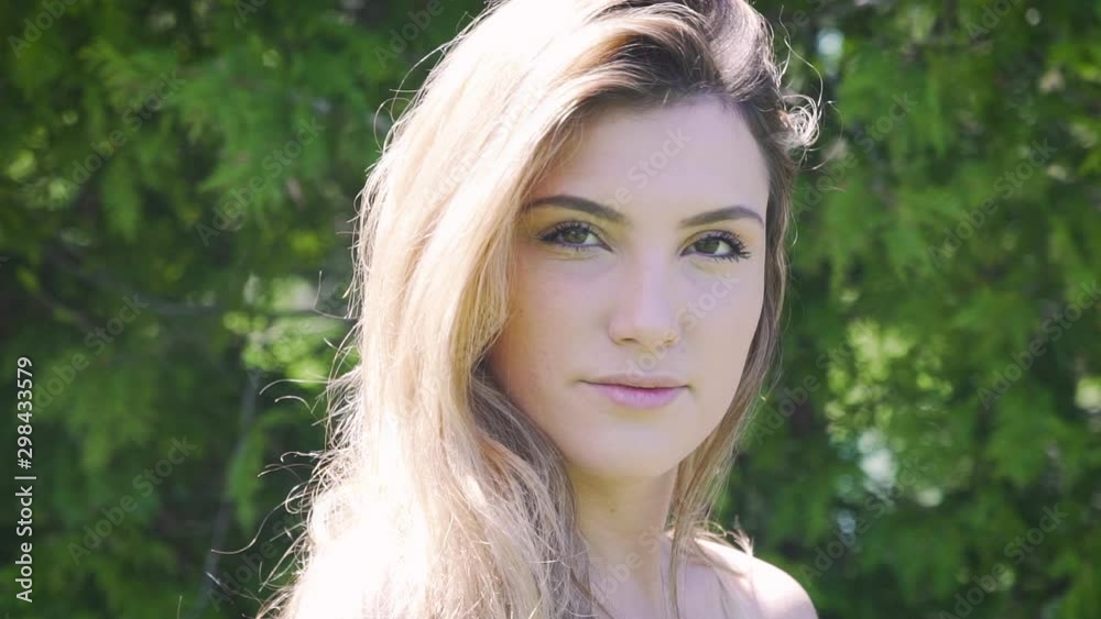 Portrait close up shot of a young blonde woman in the sunshine. Looks at camera and then walks away Portrait close up shot of a young blonde woman in the sunshine. Looks at camera and then walks away