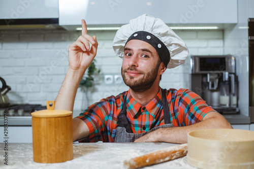Happy man in the kitchen looks with his finger up at a table with flour.
