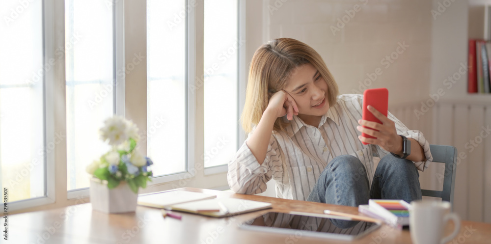 Young beautiful female designer looking at smartphone and sitting on the chair Young beautiful female designer looking at smartphone and sitting on the chair