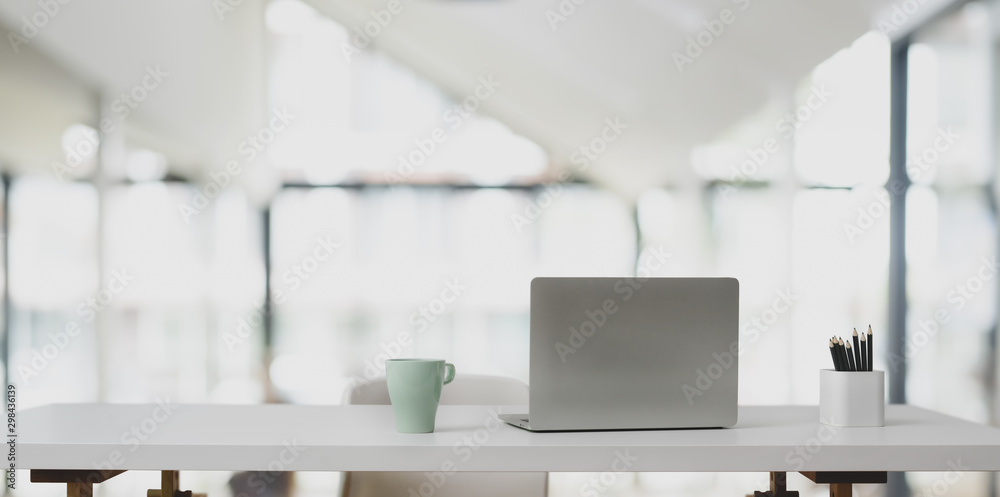 Laptop computer on white table and coffee cup in modern office with blurred background Laptop computer on white table and coffee cup in modern office with blurred background