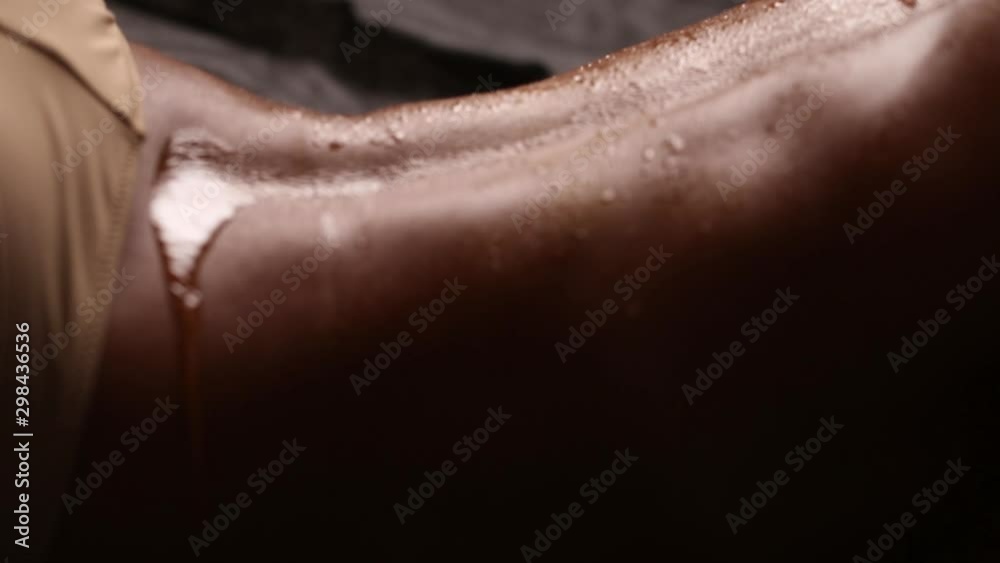 Female back with tanned skin on a black background. Drops of water on the body. Flesh-colored underwear. Grapefruit juice pours onto the skin.
