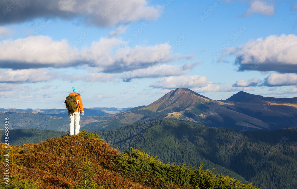 The happy tourist with the back pack stays on the hill. Autumn sunny day. Girl in sport clothes. Landscape of the mountains. Touristic place Carpathian, Ukraine Europe.