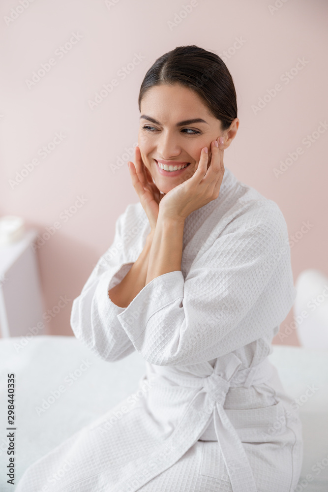 Charming young woman touching her face and smiling Charming young woman touching her face and smiling