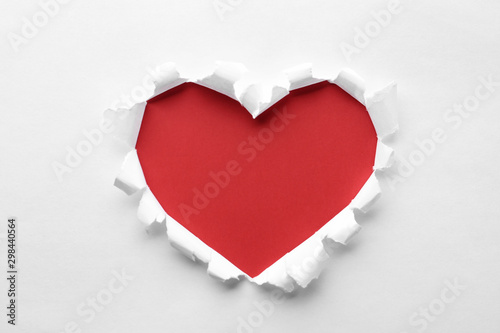 Torn heart shaped hole in white paper, top view. Red space for text