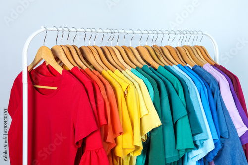 Rack with bright clothes on light blue background. Rainbow colors