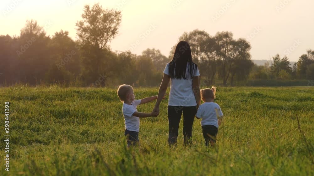 A young mother walks with her children on the green grass. Happy family having fun spending their day off in the fresh air. A young mother walks with her children on the green grass. Happy family having fun spending their day off in the fresh air.