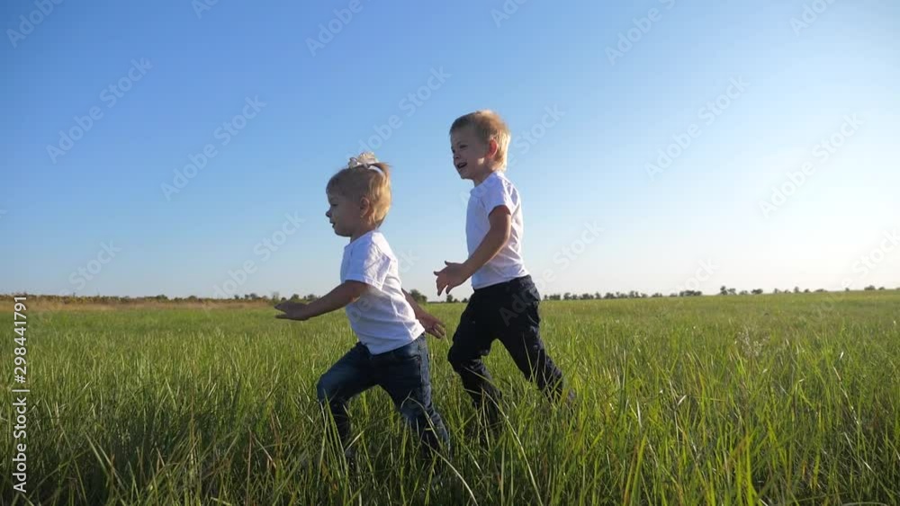Small children run on the green grass on a summer day. Blond brother and sister have fun outdoors. Small children run on the green grass on a summer day. Blond brother and sister have fun outdoors.