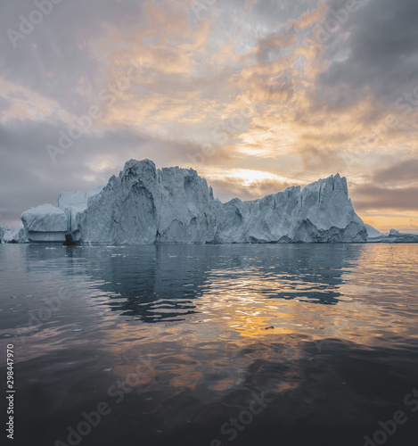 Arctic nature landscape with icebergs in Greenland icefjord with midnight sun sunset sunrise in the horizon. Early morning summer alpenglow during midnight season. Ilulissat, West Greenland.