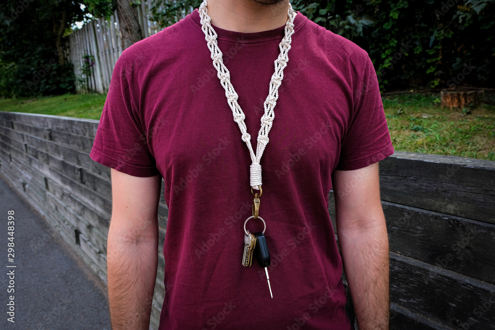 A man is wearing a long macrame keychain / lanyard around his neck that is  hanging down the front of his body. Stock Photo | Adobe Stock