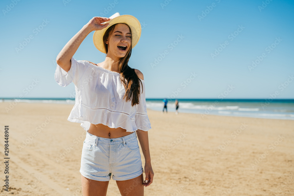 girl laughs out loud on the beach, holding her hat on her hand