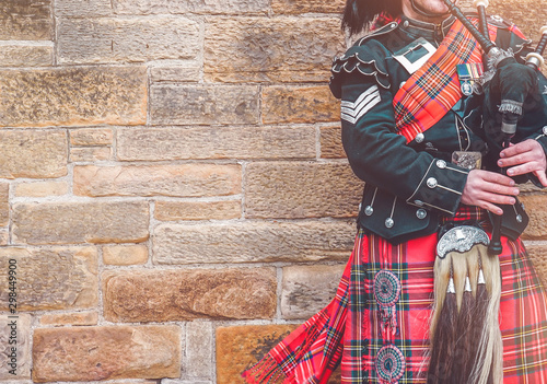 EDINBURGH, SCOTLAND, 24 March 2018 , Scottish bagpiper dressed in traditional red and black tartan dress stand before stone wall. Edinburgh, the most popular tourist city destination in Scotland..