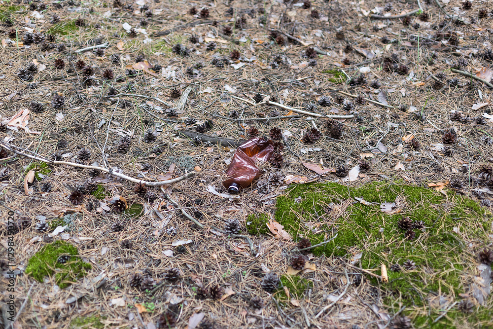 Brown plastic bottle on the ground in a pine forest. Brown plastic bottle on the ground in a pine forest.