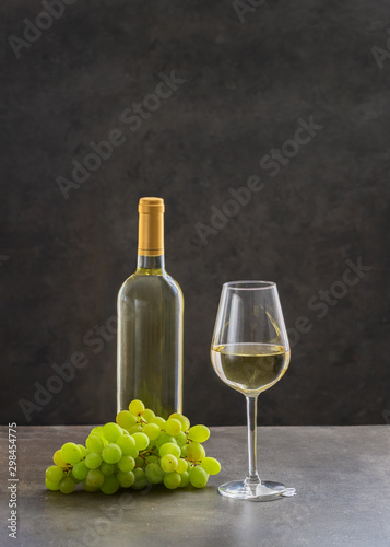 Wine bottle with white wine glass and white grapes on concrete background. Types of wine concept.