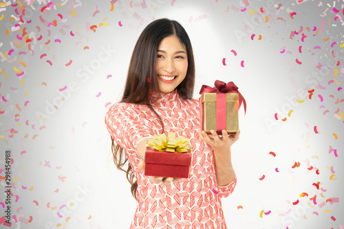 Photo of asian curious woman in red dress rejoicing her birthday or new year gift box. Young woman holding gift box with red bow being excited and surprised holiday present isolated white background