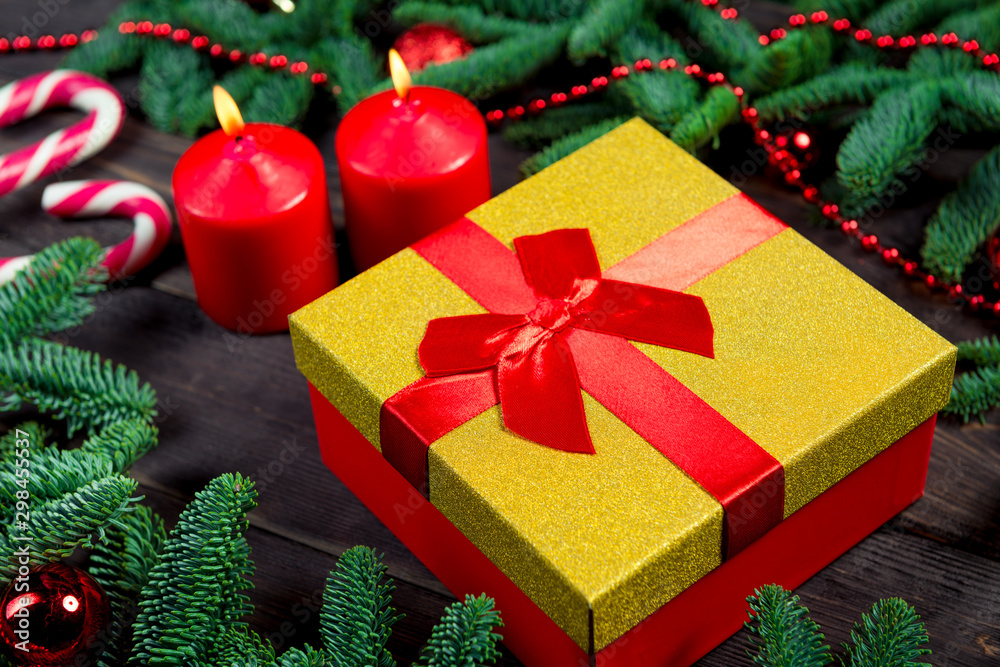 Gift with a red ribbon, burning candles and green branches of spruce on a wooden table Gift with a red ribbon, burning candles and green branches of spruce on a wooden table