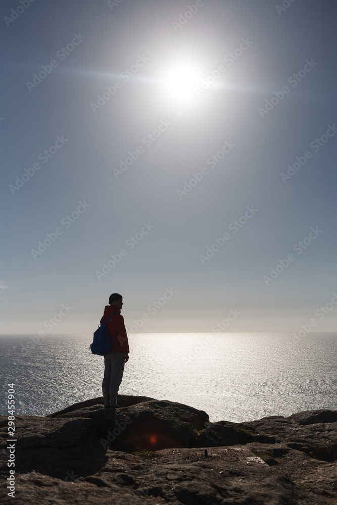 silhouette of man standing at Cape Finisterre with ocean and sun on background