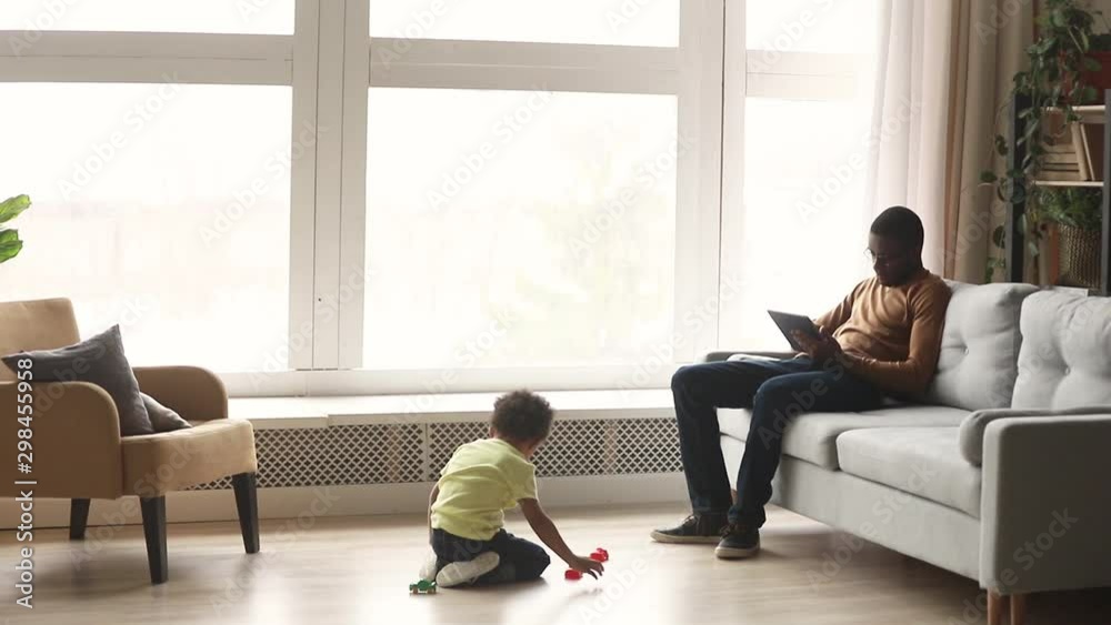 While african son play on floor father working on tablet While african son play on floor father working on tablet