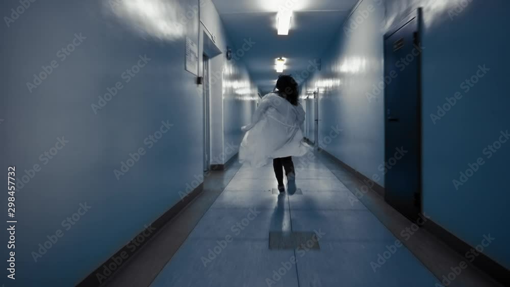 Tracking shot of zombie woman with black hair in laboratory coat walks down dark corridor goes behind door and falls,view from back. Above doorway inscription in Russian exit. Tracking shot of zombie woman with black hair in laboratory coat walks down dark corridor goes behind door and falls,view from back. Above doorway inscription in Russian exit.