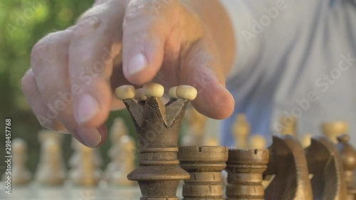 Old man prepares the chess game outside in the garden at the table and puts the black figures on their position on the board.