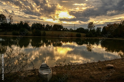 Incredible sunset view over a serene country pond with a canoe in foreground