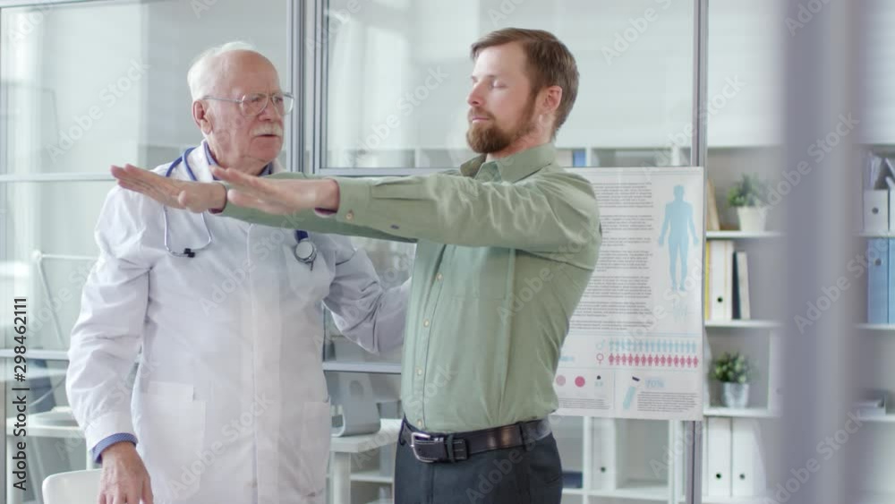 Young caucasian man standing with arms raised and eyes closed and then touching nose and clenching fists while senior neurologist examining him during medical checkup in clinic Young caucasian man standing with arms raised and eyes closed and then touching nose and clenching fists while senior neurologist examining him during medical checkup in clinic