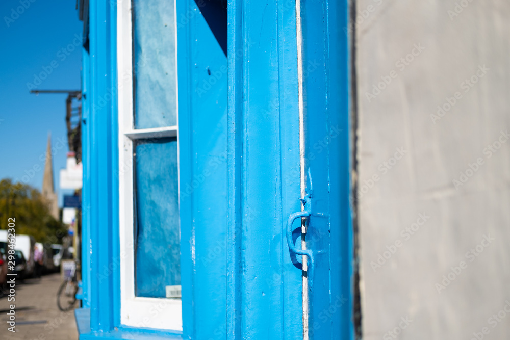 Freshly, blue painted front door and window frame seen on a terraced house, near a high street in the UK. The old, iron latch leads to a side entrance.