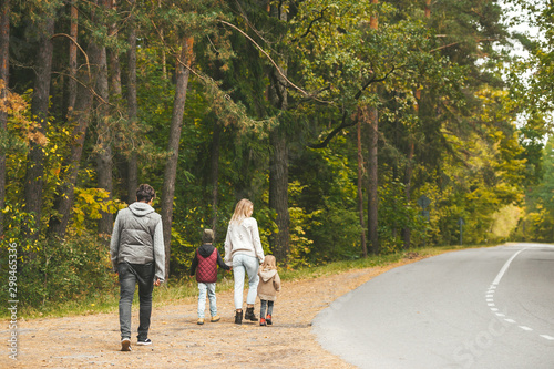 Mom, dad and little childrens, walking on country road. They are talking and enjoying beautiful autumn day.