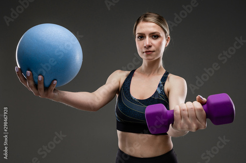 Young sports girl with long blonde hair sealed in tail, beautiful appearance, sports body, in top and legins, holds sports equipment, gantel and ball photo