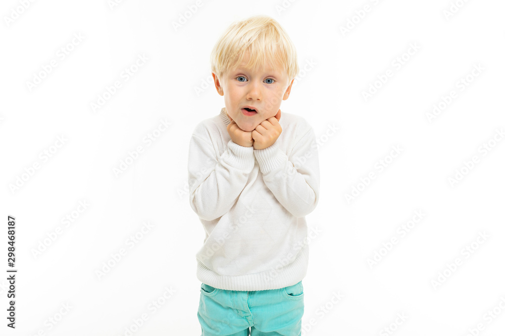 Little boy with short blonde hair, blue eyes, cute appearance, in white jacket, light blue pants, stands and is surprised Little boy with short blonde hair, blue eyes, cute appearance, in white jacket, light blue pants, stands and is surprised