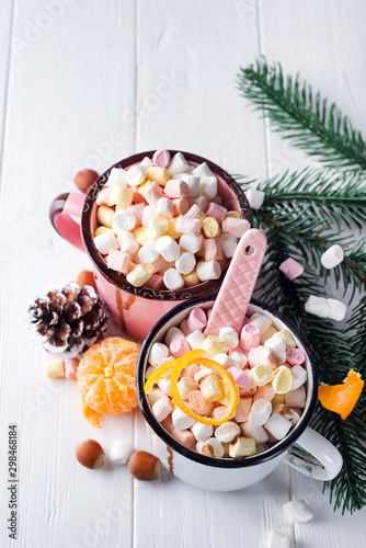 Cups of hot chocolate with marshmallows, mandarin, fir tree branches and nuts on white wooden background
