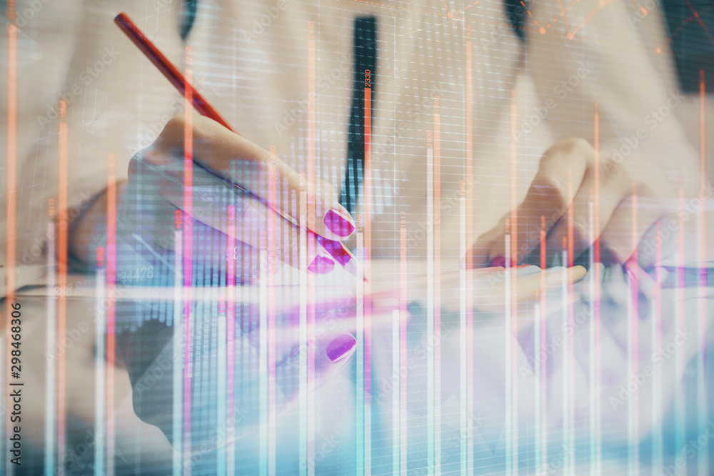 A woman hands writing information about stock market in notepad. Forex chart holograms in front. Concept of research.