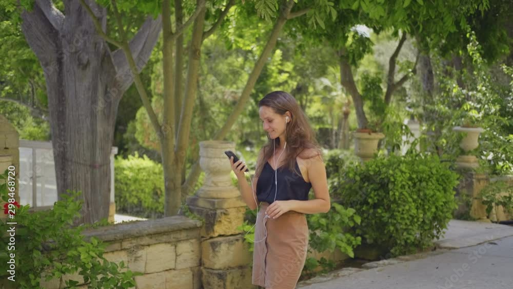 Young brunette woman in headphones communicates by video calling in the park Young brunette woman in headphones communicates by video calling in the park