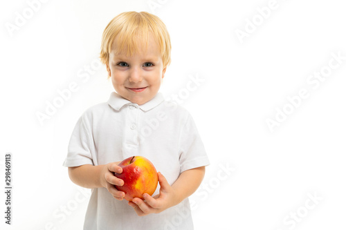 Little boy with short red hair, blue eyes, cute appearance, in white jacket, light blue pants, stands with a big red-yellow apple