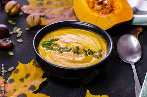 pumpkin cream soup with dark bread croutons and seeds with autumn leaves decoration on black background