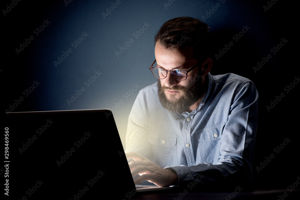 Young handsome businessman working late at night in the office with a dark background