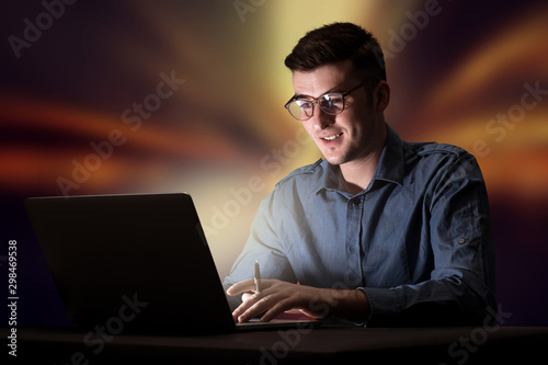 Young handsome businessman working late at night in the office with warm lights in the background © ra2 studio