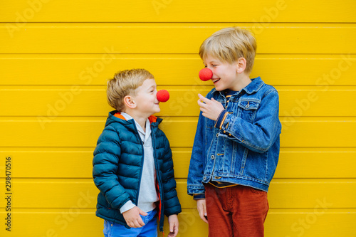 Red Nose Day Concept. Happy little brothers wearing red clown noses having fun together on sunny autmn day outdoor, yellow background. photo