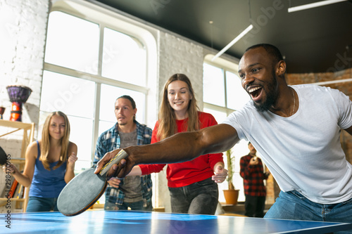 Young people playing table tennis in workplace, having fun. Friends in casual clothes play ping pong together at sunny day. Concept of leisure activity, sport, friendship, teambuilding, teamwork. photo