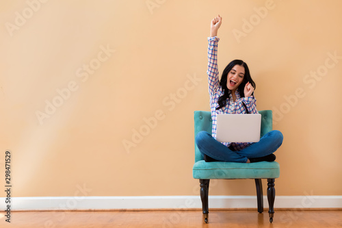 Young woman with a laptop computer with successful pose sitting in a chair