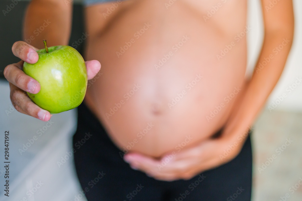 Pregnant young woman holding and showing an apple at home Pregnant young woman holding and showing an apple at home
