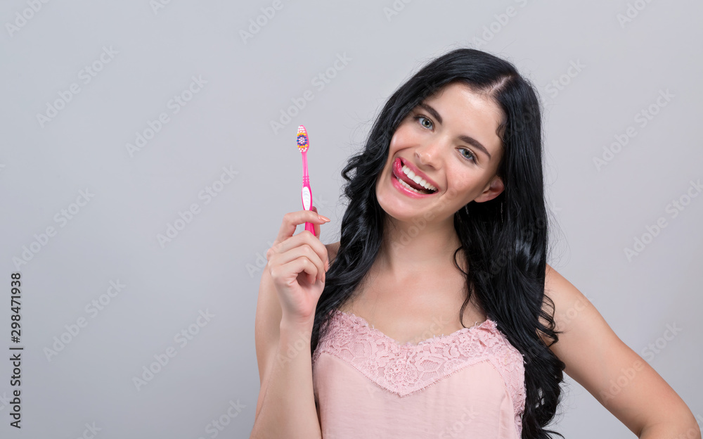 Young woman holding a toothbrush on a gray background Young woman holding a toothbrush on a gray background
