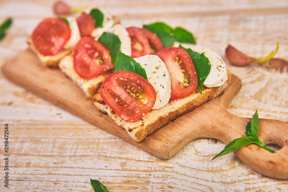Caprese bruschetta toasts on a cutting board. Bruschetta with tomatoes, mozzarella cheese and basil on a rustic table. Traditional italian appetizer or snack, antipasto