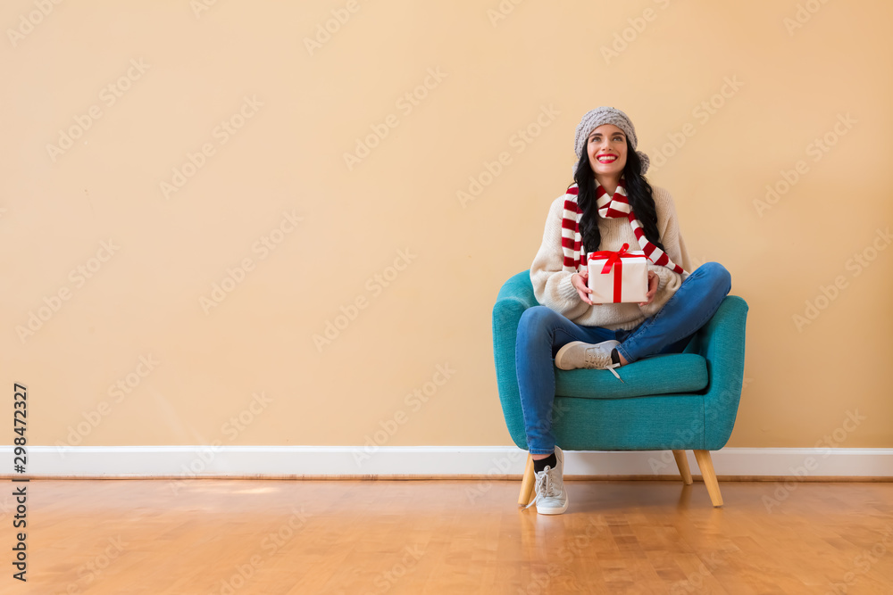 Young woman holding a gift box sitting in a chair Young woman holding a gift box sitting in a chair