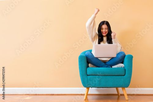 Young woman with a laptop computer with successful pose sitting in a chair photo