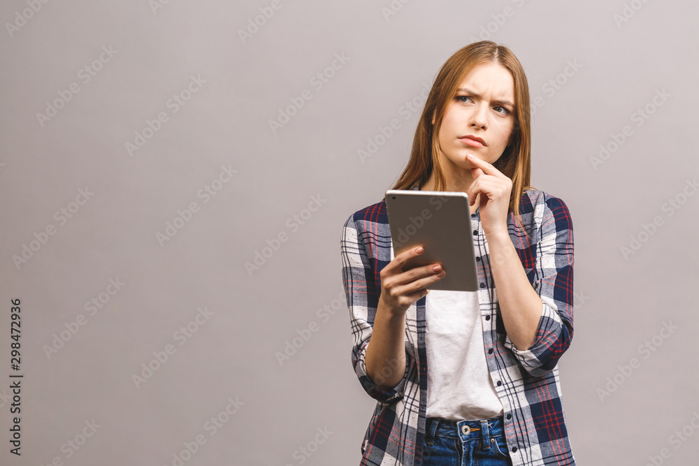 Serious thinking beautiful young woman in casual using digital tablet isolated over grey background. Serious thinking beautiful young woman in casual using digital tablet isolated over grey background.