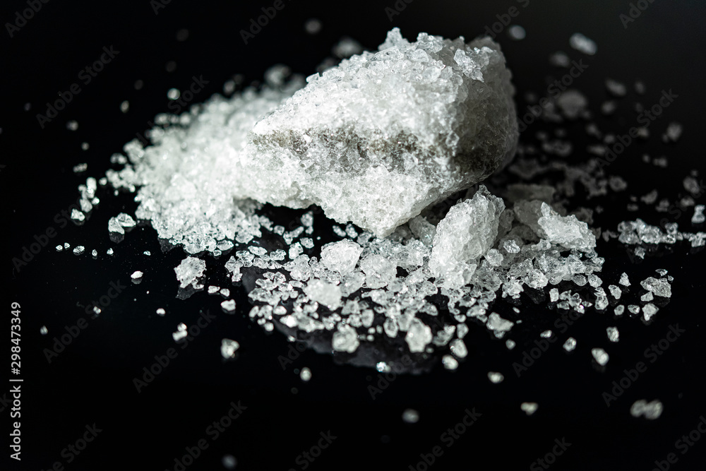 Large crystal of salt on black reflective surface; selective focus; natural edible salt Large crystal of salt on black reflective surface; selective focus; natural edible salt