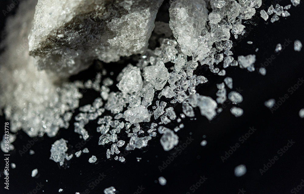 Large crystal of salt on black reflective surface; selective focus; natural edible salt Large crystal of salt on black reflective surface; selective focus; natural edible salt