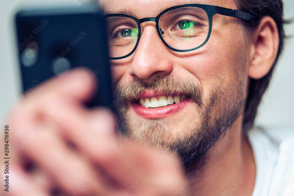 Handsome smiling young man with glasses looking at his mobile phone. Handsome smiling young man with glasses looking at his mobile phone.