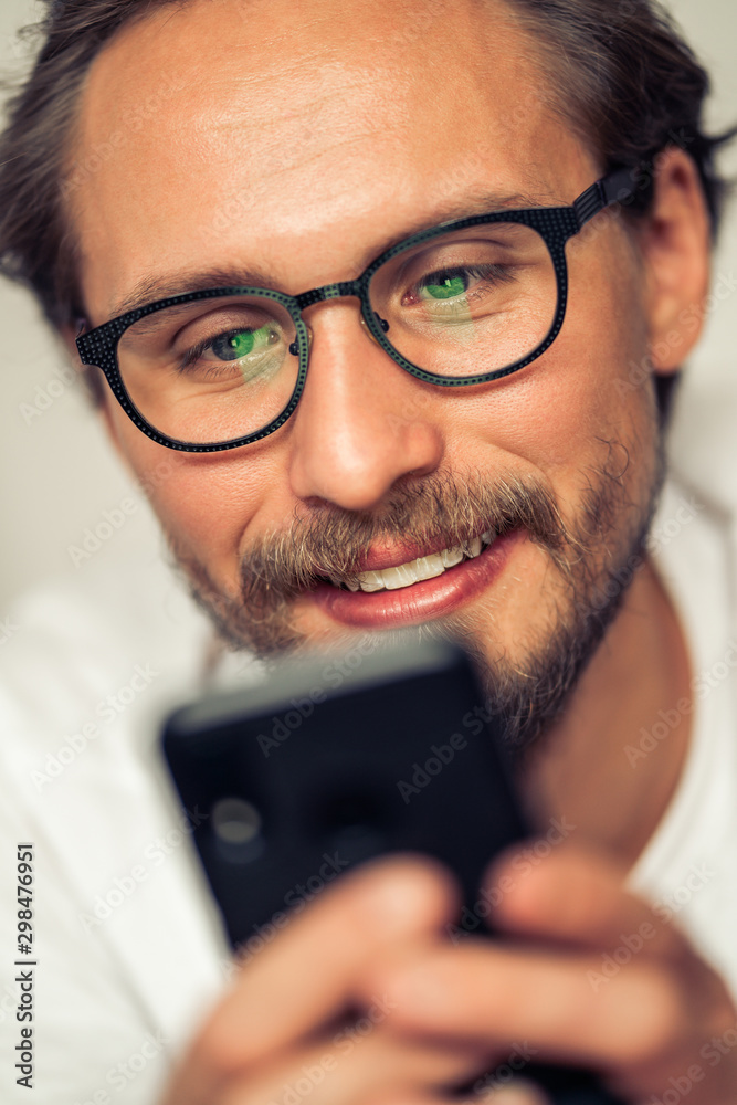 Handsome smiling young man with glasses lying on bed while holding his mobile phone. Handsome smiling young man with glasses lying on bed while holding his mobile phone.